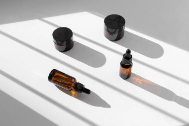 Beyaz arka planda pipetli kahverengi damlacıklı cam şişeler ve gölgeli kavanozlar. Sıfır çöp konteynırı. Serum, yağ, asit, losyon. Organik, doğal kozmetik. Spa, güzellik, cilt bakımı