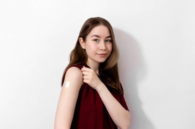 Tişörtünde Coronavirus aşısından sonra omuzlarında alçı olan gülümseyen genç bir kadın, beyaz arka plan, fotokopi alanı. Aşı, aşı, grip önleme konsepti. Covid-19 aşısı alınıyor