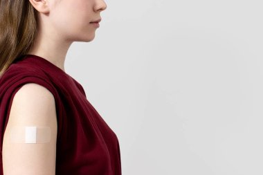 Tişörtünde Coronavirus aşısından sonra omzunda alçı olan gri arka plan, fotokopi alanı olan tanınmamış bir kadın var. Aşı, aşı, grip önleme konsepti. Covid-19 aşısı alınıyor