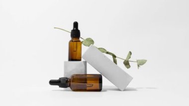Üzerinde okaliptüs dalı olan damlatan cam pipet şişeleri, kaidesel hareket animasyonu, beyaz arka plan. Serum, podyumda asit. Doğal kozmetik. Spa, güzellik, cilt bakımı