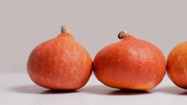 Moving picture of three orange pumpkins on white table in front of gray background side view, copy space. Autumn harvest composition. Halloween decorations, thanksgiving holidays