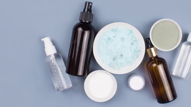 Moving picture of sea salt, serum in brown dropper glass and spray bottle, clay mask, jar of cream flat lay on blue background top view. Organic, natural cosmetic. Beauty, skincare, spa product — Stok video