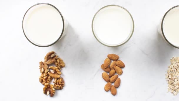 Motion picture of glass of almond, walnut, oat milk on marble background top view. Nut vegan milk. Lactose-free, dairy free milk. Hypoallergenic drink. Healthy diet and nutrition — Stock Video