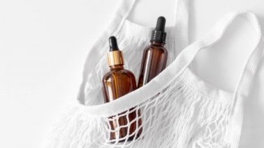 Serum, asit, kahverengi damlacık bardakta losyon ve beyaz üzerine konulmuş ağ torbası pipetinin hareketli resmi. Çevre dostu, yeniden kullanılabilir alışveriş çantası. Organik, doğal kozmetik. Güzellik, cilt bakımı. Sıfır..