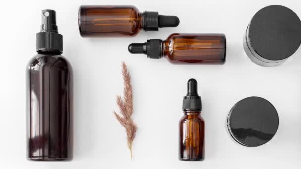 Rörlig bild av kit av bruna glasflaskor och burkar platt låg med pampas gräs på vitt. Noll avfall eco glasbehållare. Serum, olja, syralösning. Ekologisk, naturlig kosmetika. Skönhet, hudvård koncept — Stockvideo