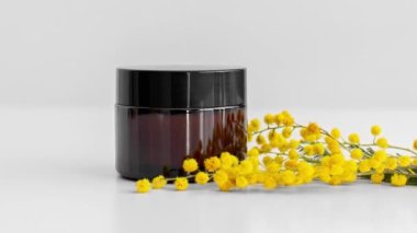 Krema, serum, kahverengi cam kavanozda yağ ve sarı mimoza çiçeği, bej arka plan. Sıfır atık eko cam kap. Spa ürünü. Organik, biyolojik, doğal kozmetik. Güzellik, cilt bakımı.