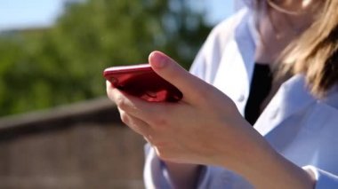 Kadın eli akıllı telefona dokunuyor, caddede yayın yapıyor. Cihaz kullanan gömlekli genç bir kadın. Şehir tarzı ve sokak modası. Akıllı telefondan mesaj atan bir kız. Sohbet, mesajlaşma, okuma..