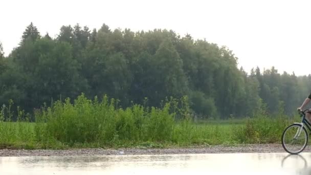 Młody człowiek samotnie jeździ na rowerze na wsi w deszczową pogodę na tle lasu. Aktywność letnia, zdrowy tryb życia, trening, sport, fitness. Samotna osoba w naturze. Zabawa na świeżym powietrzu. — Wideo stockowe