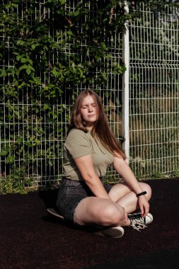 Dışarıdaki kaykayda oturan şortlu, gözleri kapalı genç bir kadın. Yaz aktivitesi, sağlıklı yaşam tarzı, egzersiz, spor, spor, spor, binicilik. Doğada yalnız bir insan. Dışarıda eğleniyoruz..