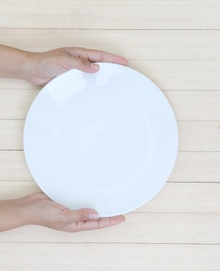 Kadın el boş beyaz tabak tahta ahşap arka plan üzerinde tutarak.