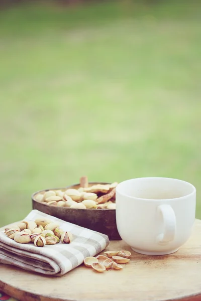 Pistachio nut and white coffee cup on wood background. — Stock Photo, Image