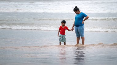 Weligama, Sri Lanka - 07: 26: 2020: Anne, oğlunun elini sahilde tutuyor, suyu yansıtıyor.