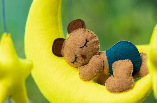 Dreamy baby crib mobile closes up, hangs over the baby bed, cute bear sleeping on the yellow moon, stuffed fluffy felt handmade cot toy for newborn baby.