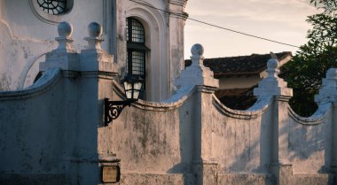 Eski sömürge kilise binası ve beyaz duvarların dışında akşam ışığı duvarı aydınlatırken odak noktası sokak lambası olan.
