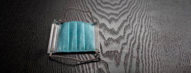 Bir cerrahi maske, koyu ahşap bir masanın üstüne, koronavirüs önleme konsepti olan fotokopi alanı ile yassılaşmıştı..