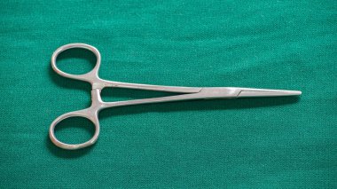 Yeşil giysili bir masa üstünde tek parça Hemostatik Forseps makası..