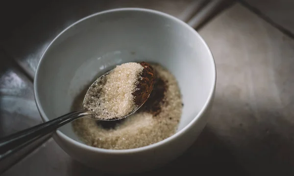 Measuring sugar and instant coffee powder by tablespoon into a white bowl. preparing ingredients for making Dalgona coffee foam. a spoonful of sugar and coffee mixture overhead close up view.