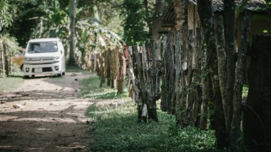 Tahta çitler, çakıllı yolun sonundaki park halindeki arabaya giden yolu gösteriyor..