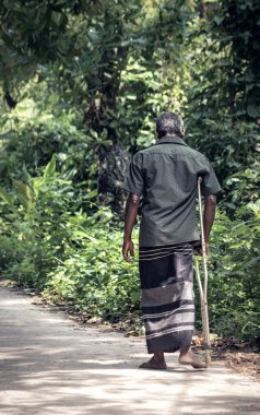 Köyün ıssız bir kırsal kesiminde yaşlı bir yetişkin bir sopayla yürüyor..