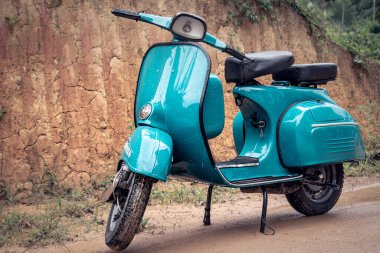 Vespa Scooter önü, yağmurlu bir günde çamurlu bir yolda park edilmiş. Gökyüzü mavisi klasik motosiklet.