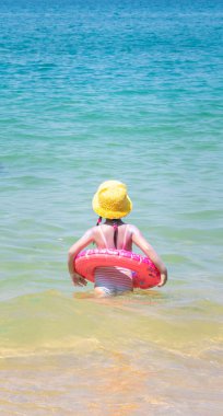 Etrafında hava tüpü olan küçük bir çocuk, sakin okyanus sularında sarı şapka ve canlı mavi renkler takıyor..
