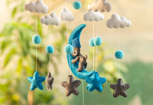 Baby crib hangings, Felt cot mobile made with plush clouds, moon, and stars. Space-themed handmade hanging close up against soft blurred background.