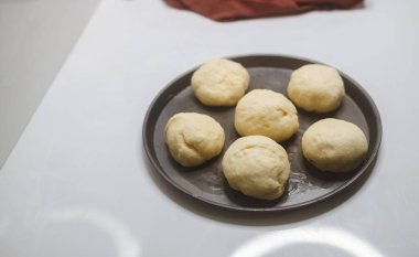 Flour dough balls resting on an oily surface on the round pizza plate in the home kitchen. Dough balls have perfectly risen. Hand kneaded the dough for making homemade pastry buns to bake in the oven.