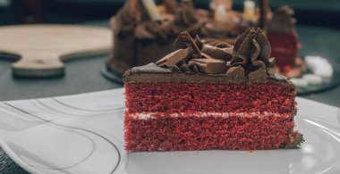 Masanın üstünde beyaz bir seramik tabakta çikolatalı pasta dilimi. Buzlu çiçekler ve çikolata parçalarını malzeme olarak kullanmak. Lezzetli Buzlu Doğum günü pastası tasarımı yakın plan görünümü.