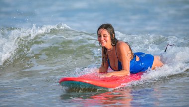 Weligama, Sri Lanka - 10 11 2022: Sörf tahtasında uzanan ve akşamları sörf yapmaktan zevk alan çekici beyaz kız. Mavi bir mayo giyen dişi sörfçü.