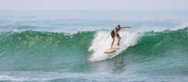 Mirissa, Sri Lanka - 04: 15: 2023: siyah dalgıç kıyafetli beyaz erkek sörfçü Mirissa sahilinde yeşil bir dalga sürüyor..