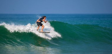 Mirissa, Sri Lanka - 04: 15: 2023: Mirissa sahilinde yeşil dalgada sörf yapan siyah dalgıç kıyafetli beyaz erkek.