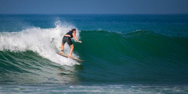 Mirissa, Sri Lanka - 04: 15: 2023: Mirissa sahilinde yeşil bir dalgaya binen siyah dalış kıyafetli beyaz erkek sörfçü.