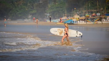 Weligama, Sri Lanka - 04 19 2023: Bikinili sarışın kız uzun bir sörf tahtası taşıyor ve denize doğru yürüyor,
