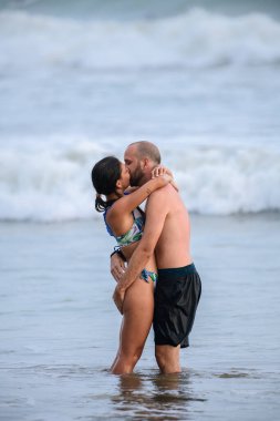 Weligama, Sri Lanka - 04 23 2023: A couple embraces passionately in the shallow waters of the ocean, their bodies entwined as waves crash behind them, creating a romantic and intimate moment