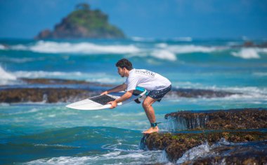 Weligama, Sri Lanka - 05 04 2023: Sörfçü kayalık bir resiften kendini suya atar ve tahtasını dengeler. Ham enerji ve tropik bir cennette mükemmel dalgayı yakalama beklentisi.