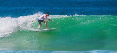 Weligama, Sri Lanka - 05 04 2024: Bir erkek sörfçü denge ve kontrol sergileyerek güçlü bir dalga üzerinde sorunsuzca süzülür. Beyaz tişört ve siyah şort giyiyor.