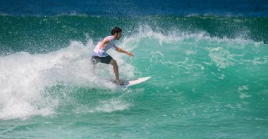 Weligama, Sri Lanka - 05 04 2024: Bir erkek sörfçü denge ve kontrol sergileyerek güçlü bir dalga üzerinde sorunsuzca süzülür. Beyaz tişört ve siyah şort giyiyor.