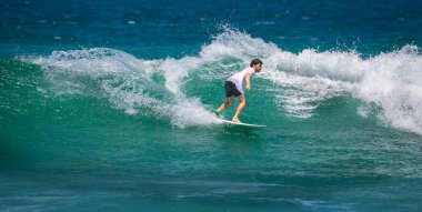 Weligama, Sri Lanka - 05 04 2024: Bir erkek sörfçü bir dalgayı güç ve hassasiyetle oyuyor. Temiz su spreyi ve dinamik hareket sürüşün heyecanını ve yoğunluğunu yakalar.