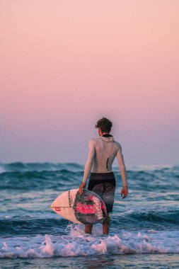 Madiha, Sri Lanka - 02: 02: 24 2025: Sörfçü, uzun kollu döküntü koruyucu ve kısa pano taşırken desenli şort giyerek sabahın erken saatlerinde sörfe giriyor..