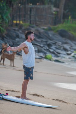 Ahangama, Sri Lanka - 02: 13 2025 Bir adam sahilde sörf tahtasının yanına uzanır..