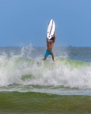 Weligama, Sri Lanka - 05: 20 2023: Açık turkuaz şortlu sörfçü kırılan bir dalganın ortasında kafasının üstünde sörf tahtasıyla yakalandı