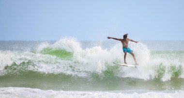 Weligama, Sri Lanka - 05: 20 2023: Patlayıcı enerjiyle dalgayı fırlatmaya hazır sörfçü. Sörfçü, sörf hareketinin dramatik bir anında elit atletizm ve stil sergiliyor