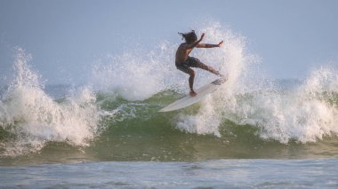 Weligama, Sri Lanka - 05: 20 2023: Zayıf, kaslı bir erkek sörfçü güçlü bir yeşil dalganın üzerinde sadece parlak mavi şortlar giyerek havadan manevra yapar..