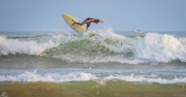 Weligama, Sri Lanka - 05: 20 2023: Renkli vücutlu yetenekli bir erkek sörfçü sarı bir sörf tahtasında havadan manevra yapar ve kırılan bir dalganın tepesini yakalar.