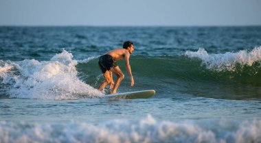 Weligama, Sri Lanka - 05: 27: 2023: Üstsüz bir erkek sörfçü sabah ışığında küçük yeşil bir dalgada sörf yaparak sörf tahtasında alçak ve sabit bir duruş sergiliyor.