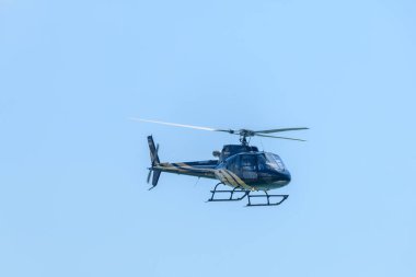 Altın çizgili siyah helikopter açık mavi gökyüzünde zarif bir şekilde süzülüyor.