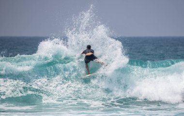 Erkek bir sörfçü büyük bir kesinti yapıyor ve yüksek dalgalara büyük miktarda su püskürtüyor.