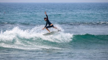 Midigama, Sri Lanka - 03 05: 2024: Formda ve atletik yapıya sahip bir erkek sörfçü, uzun kollu koyu renk döküntü koruyucu ve tahta şortlar dizisi 3-05 giyerek havada dinamik bir dönüş yapıyor