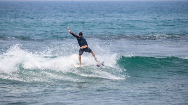Midigama, Sri Lanka - 03 05 2024: Formda ve atletik yapıya sahip bir erkek sörfçü, uzun kollu koyu renk döküntü koruyucu ve tahta şortlar dizisi 3-06 ile havada dinamik bir dönüş yapıyor