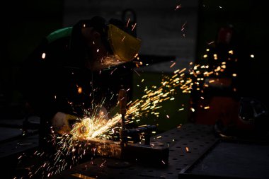 Moskova, Rusya - 06 08 2018: Kare bir metal tüpü kesmek için dairesel testere kullanan işçiler koyu arkaplanda kıvılcımlar yarattılar